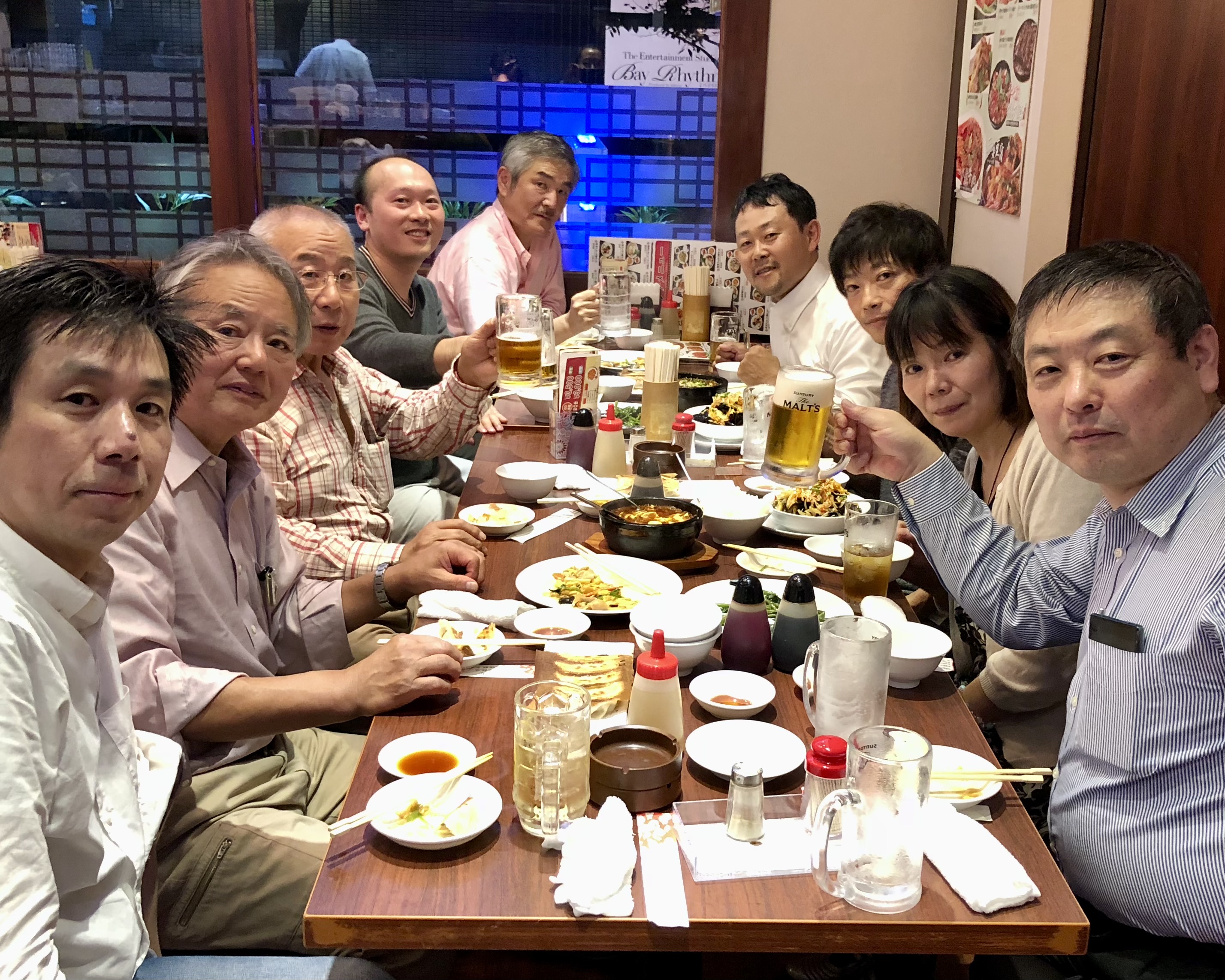 Eleven people seated around a dining table with food and drinks in a restaurant.