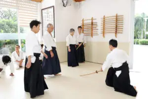 People in traditional uniforms practice with wooden swords in a bright martial arts dojo.