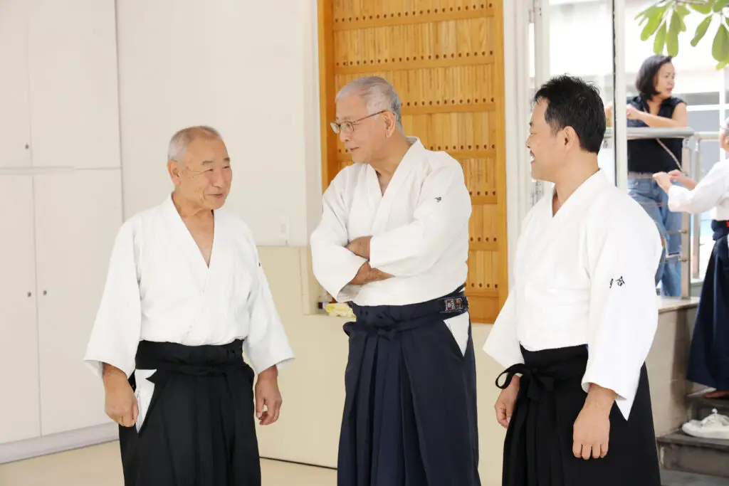 Three men in traditional martial arts attire standing indoors, engaged in conversation.