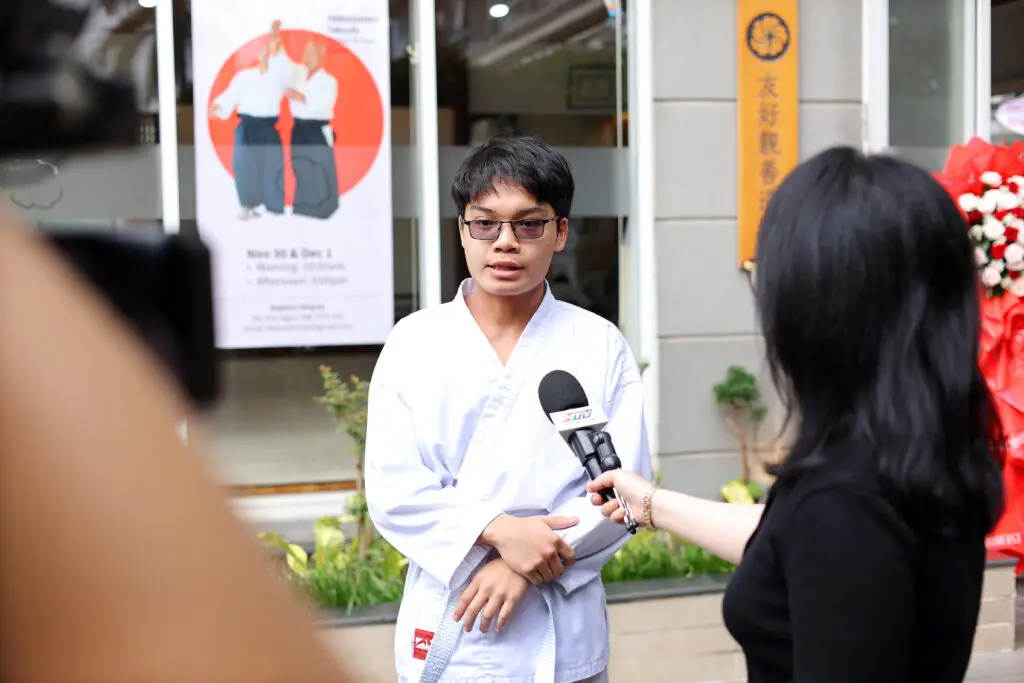 Person in martial arts uniform being interviewed outdoors with a microphone and camera.