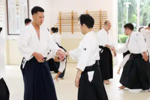 People in martial arts uniforms practicing techniques in a well-lit dojo with wooden racks.