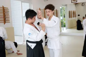 Two martial artists in traditional uniforms practicing a technique inside a dojo.