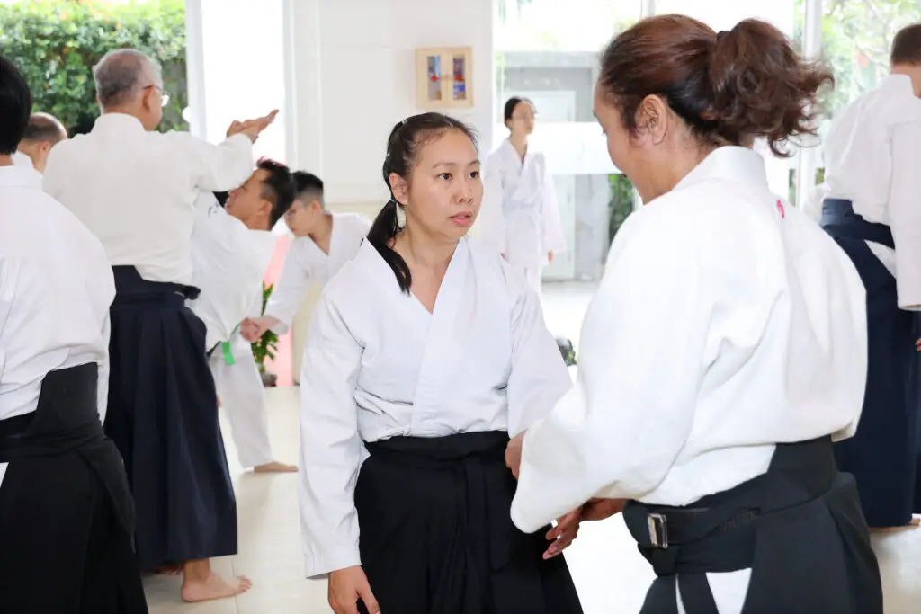 People in martial arts uniforms practicing techniques together in a well-lit training space.