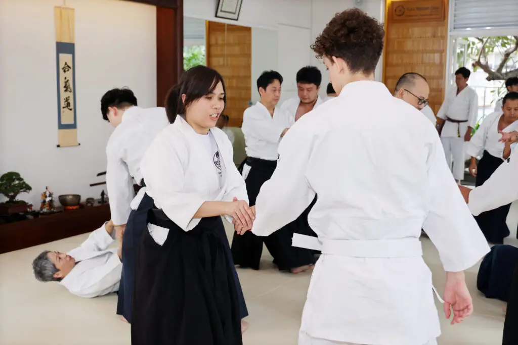 People practicing martial arts techniques in a dojo with traditional Japanese decor.