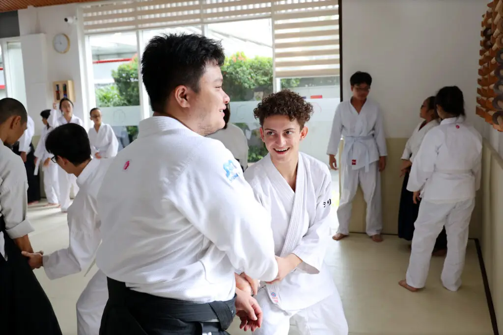 People in martial arts uniforms practicing techniques in a brightly lit dojo.