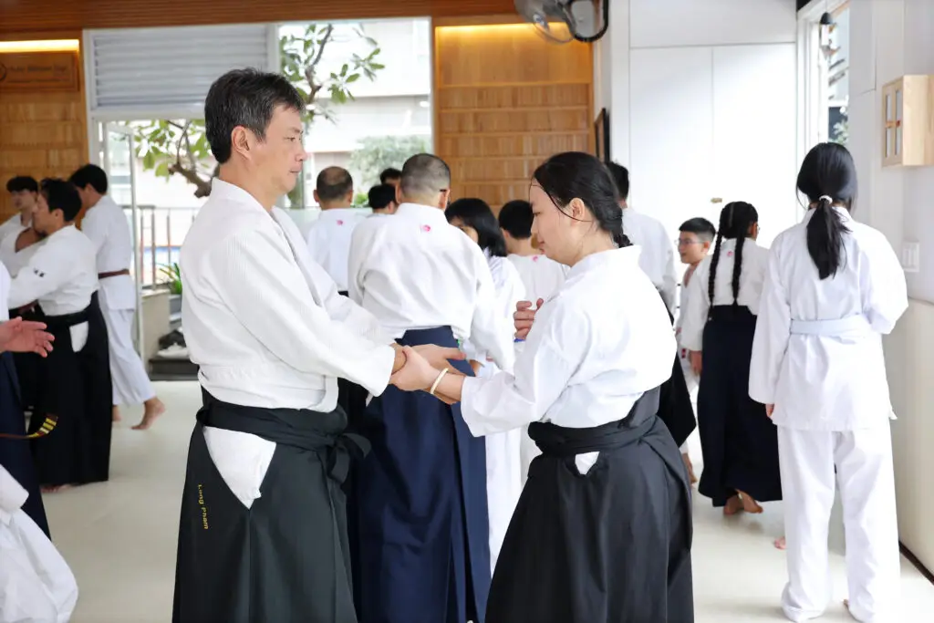 Martial arts students practicing partner wrist techniques in a bright indoor dojo setting.