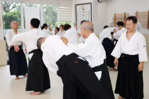 Martial arts class with students in white uniforms and black hakama practicing techniques indoors.