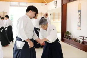 Two Aikido practitioners demonstrating a wrist lock in a traditional dojo setting.