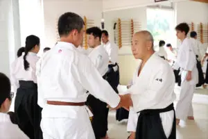 Martial arts students in a dojo practicing techniques wearing white uniforms with belts.