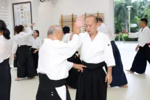 People practicing martial arts in a dojo wearing white tops and black hakama pants.