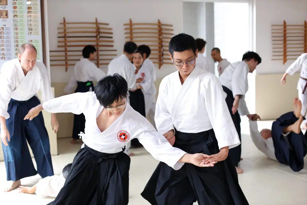 People practicing Aikido techniques in a dojo wearing traditional uniforms and hakama.