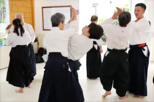 People practicing paired martial arts techniques indoors wearing white tops and dark hakama pants.