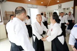 People in martial arts uniforms practicing partner techniques in a dojo with wooden weapon racks.
