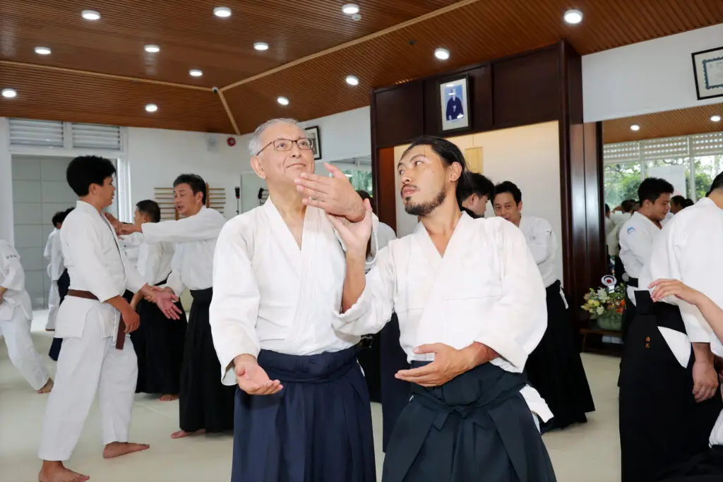 Martial arts class in a dojo with participants practicing techniques in pairs.