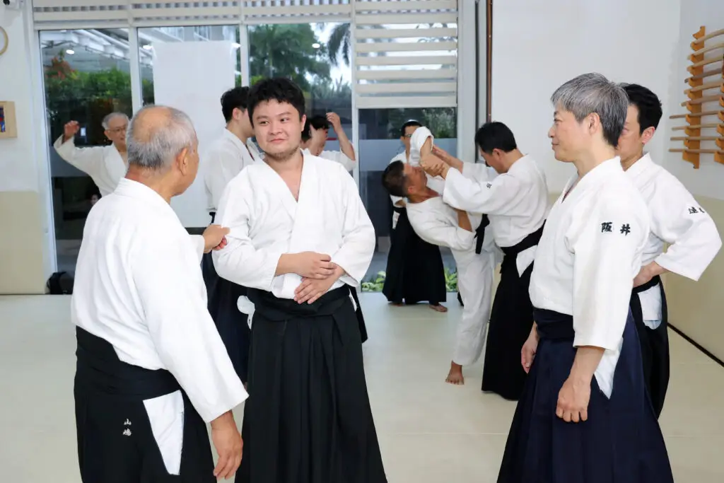 People practicing Aikido techniques and discussing in a dojo with white gi and black hakama pants.