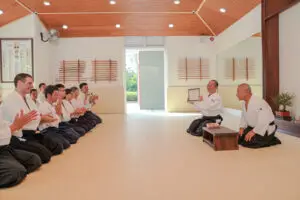 Martial arts practitioners in a dojo with wooden swords and mirrors, one holding a certificate.