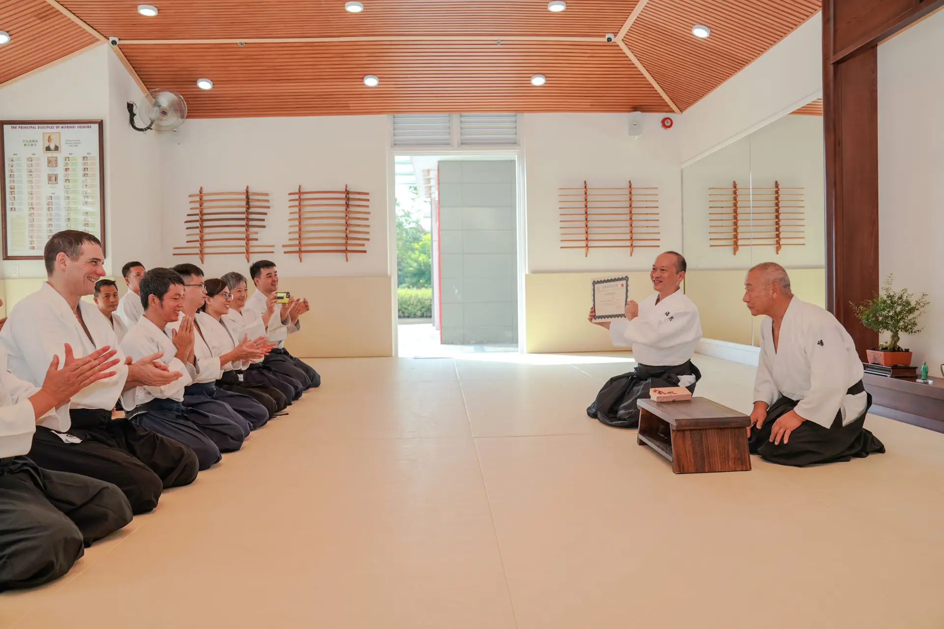 Martial arts practitioners in a dojo with wooden swords and mirrors, one holding a certificate.